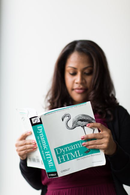 The image shows a woman with long dark hair, wearing a black blazer over a burgundy top, holding and reading a landscaping or gardening book titled 'Dynamic HTML' by O'Reilly. She appears to be focuse